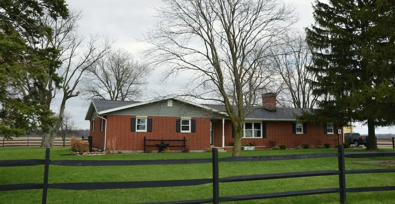 Red brick ranch house behind a dark wood fence and bare winter trees