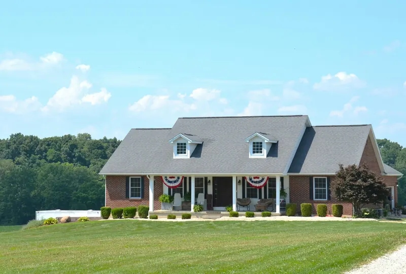 Brick house with a covered front porch and flag bunting on a wide lawn
